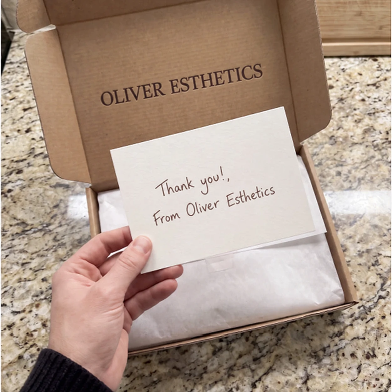 An Oliver Esthetics box, wrapped in tissue, with a handwritten thank you card