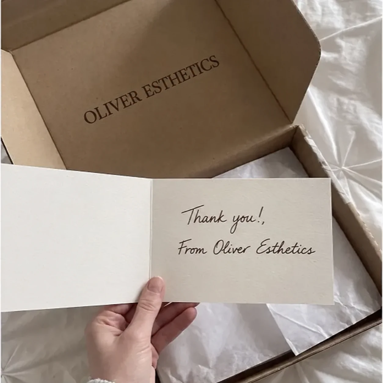 An Oliver Esthetics box, wrapped in tissue, with a handwritten thank you card